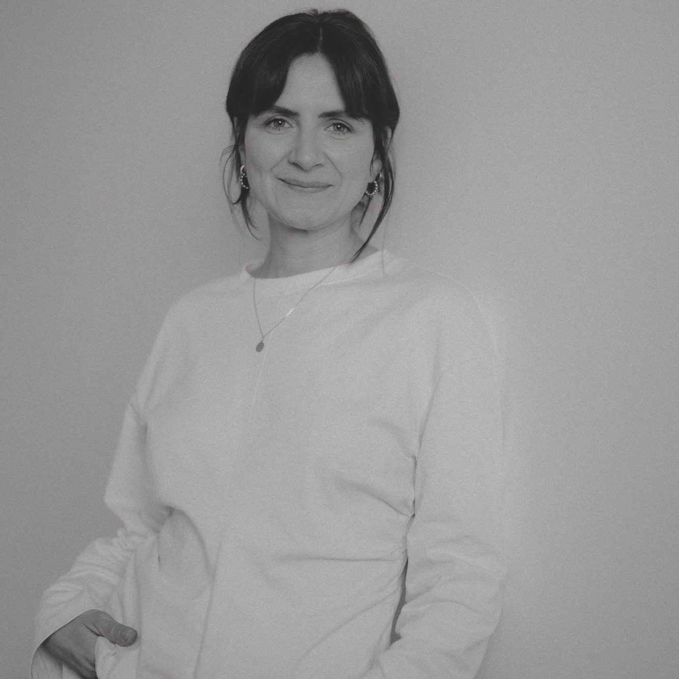 Bild von Hannah Waeny (doulannah) vor einer weißen Wand mit freundlichem Blick und einem sanften Lächeln.