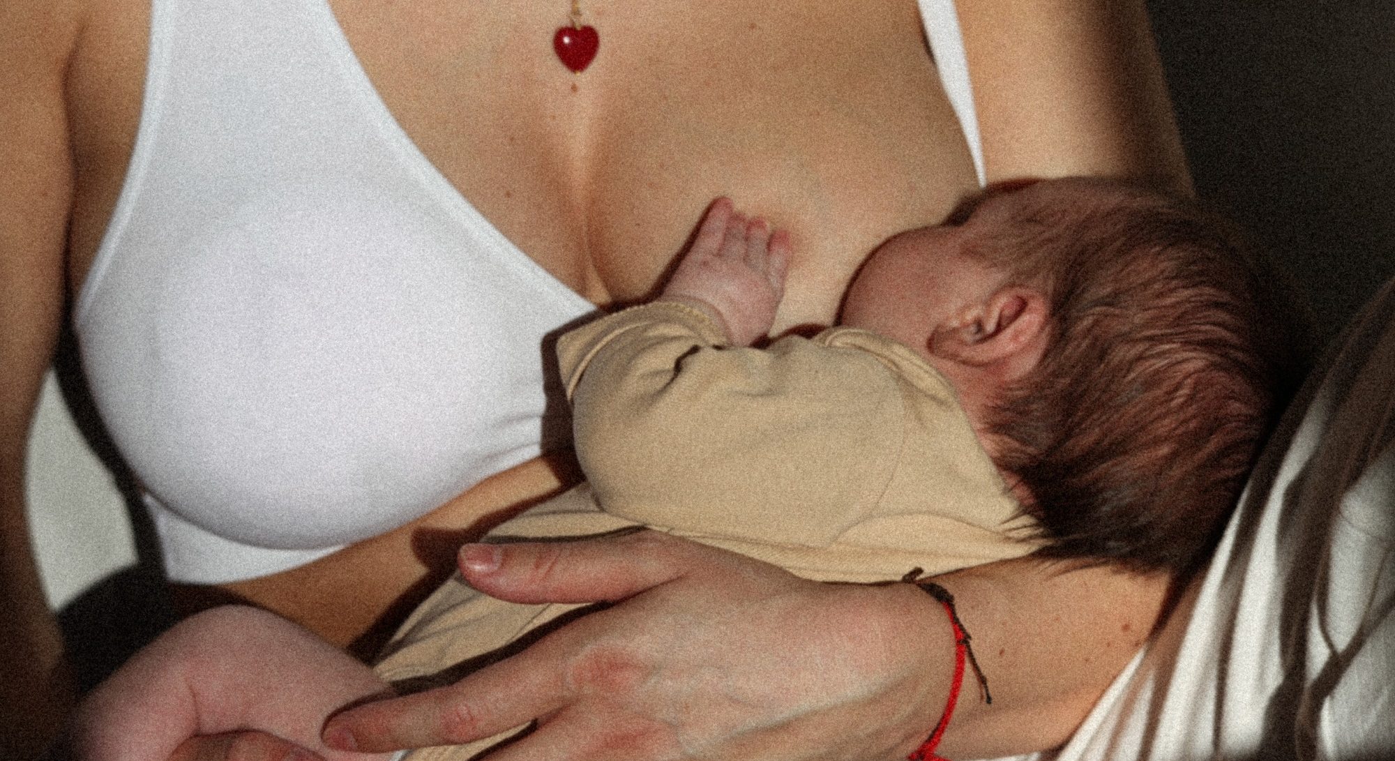 Eine Mutter trägt einen weißen Still-BH und hält ihr Neugeborenes Kind zum Stillen an die Brust. 